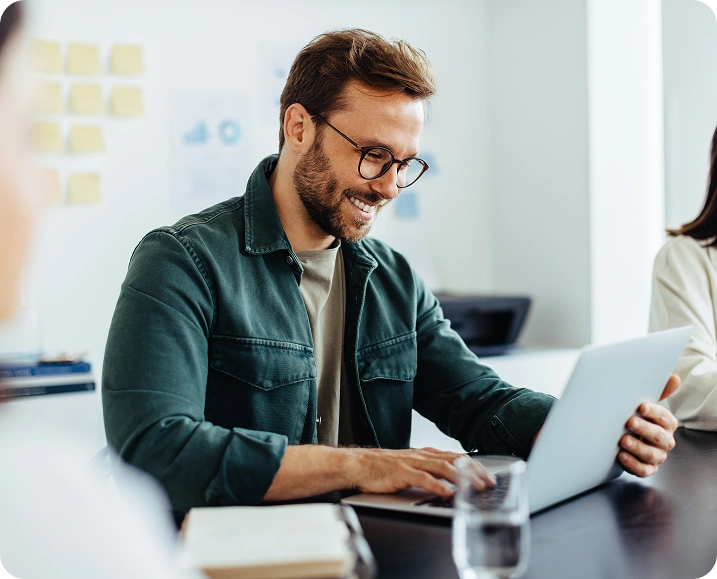Smiling-professional-man-working-on-a-laptop-in-a-bright-office-environment-seated-at-a-desk-with-documents-and-a-glass-of-water Smiling professional man working on a laptop in a bright office environment, seated at a desk with documents and a glass of water